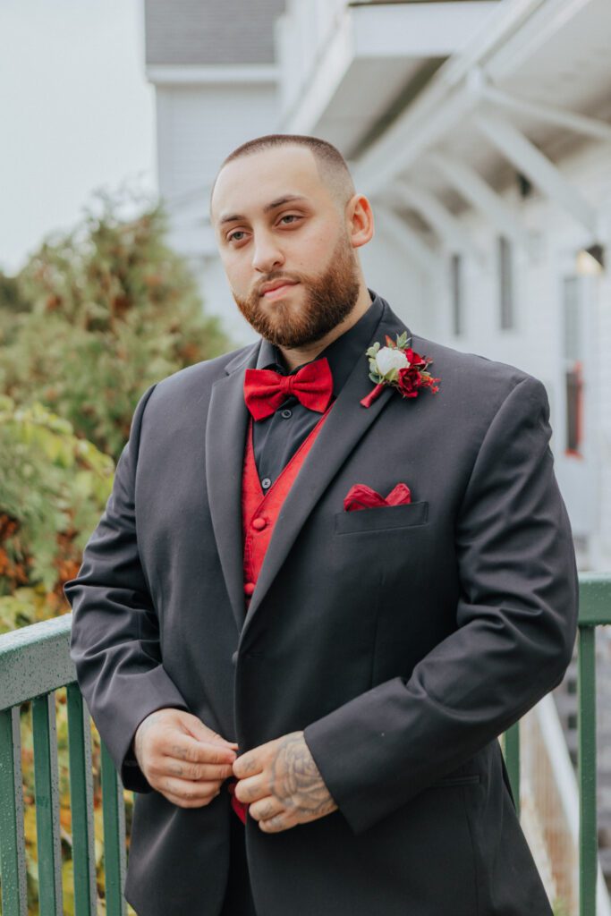 Groom buttoning his suit as he gets ready outside at Black Swan Country Club in Georgetown, Massachusetts.