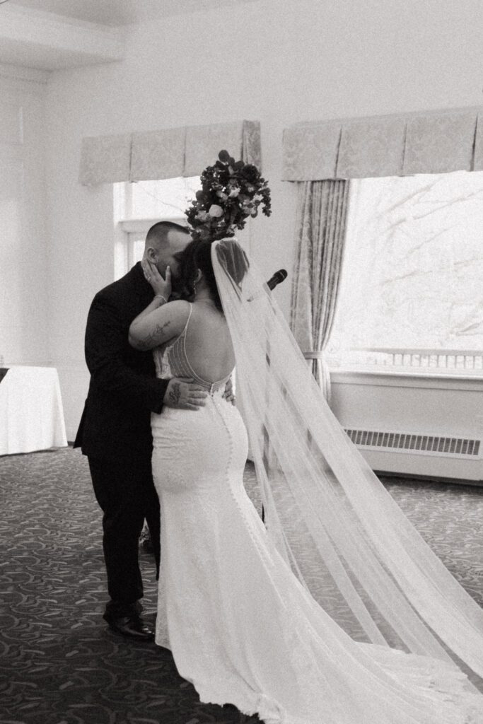 Bride and groom kissing during romantic indoor wedding ceremony at Black Swan Country Club in Georgetown, Massachusetts.