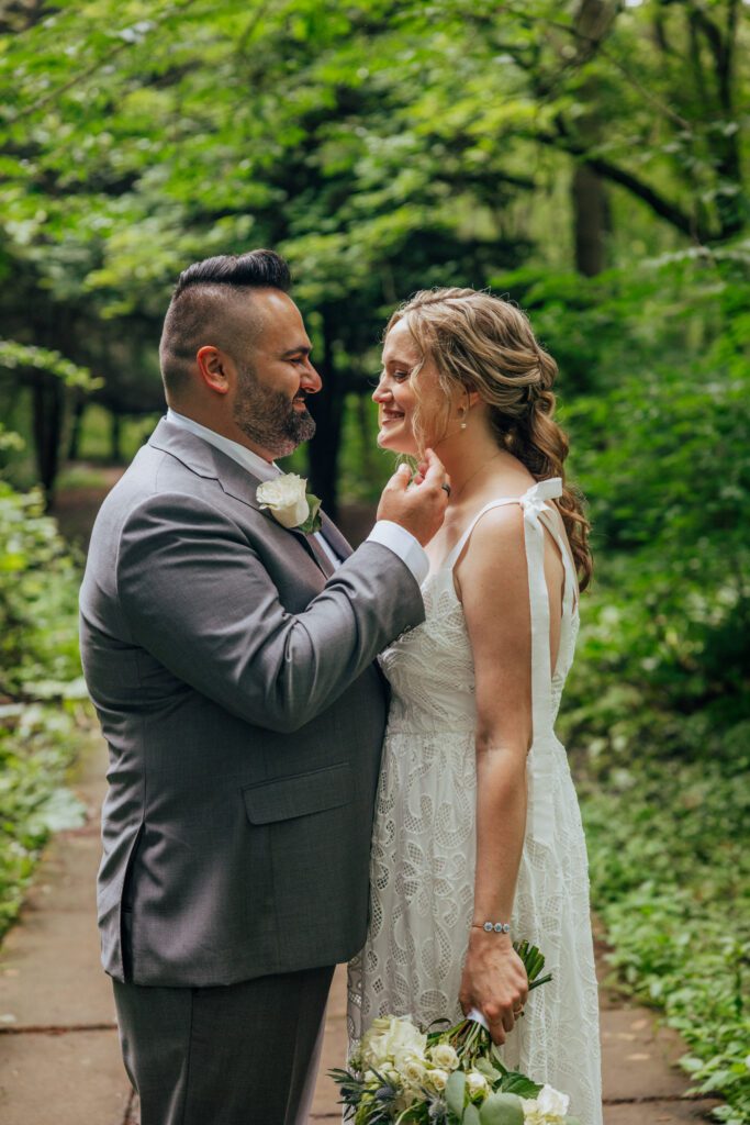 Groom moving brides hair as they smile at each in the woods at Bird Park in Walpole, Massachusetts.