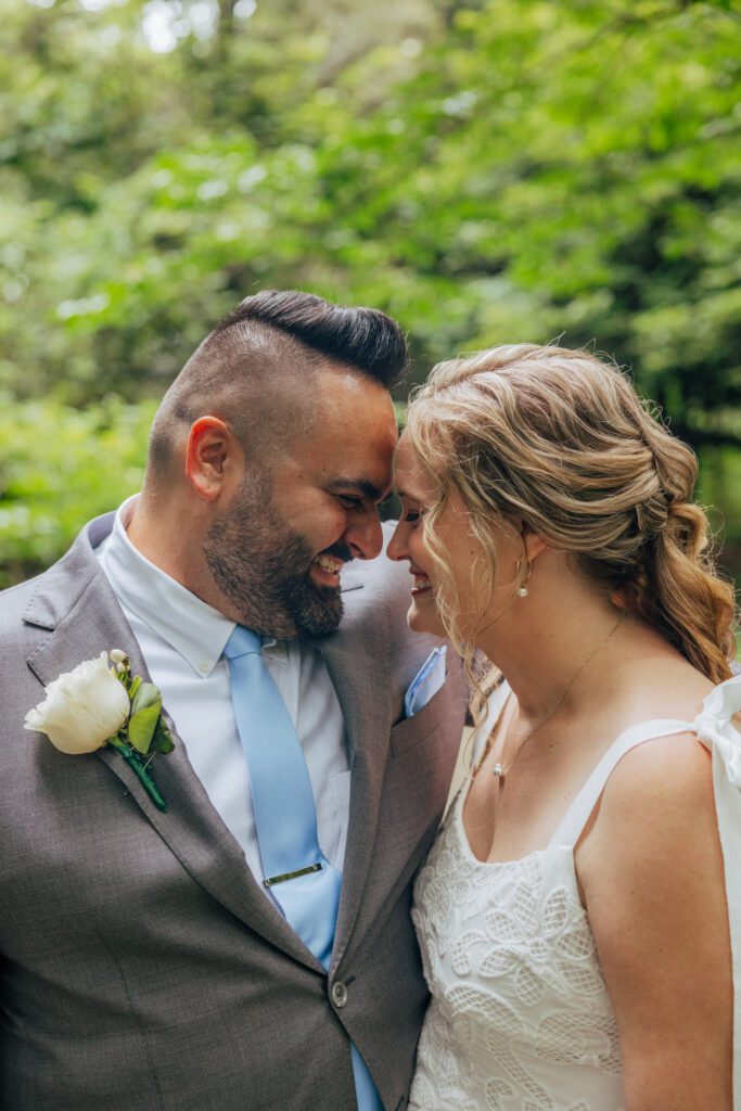 Bride and groom smiling in the woods with their heads together during their whimsical summer elopement at Bird Park in Walpole, Massachusetts.
