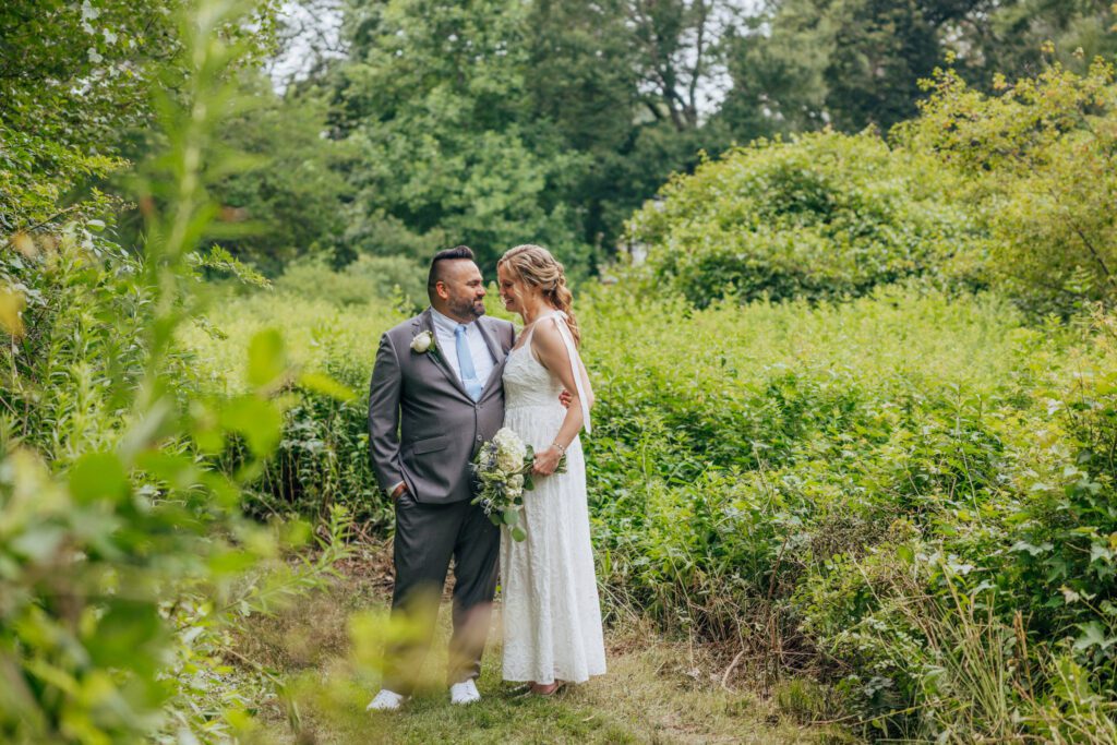 Groom and bride smiling at each other in front of a wild flower field during wedding atBird Park in Walpole, Massachusetts.