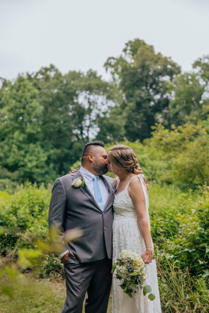 Bride and groom kissing in whimsical wild flower field during summer elopement at Bird Park in Walpole, Massachusetts.