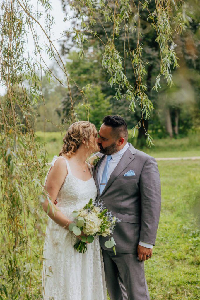 Bride and groom kissing under willow tree during elopement at Bird Park in Walpole, Massachusetts.