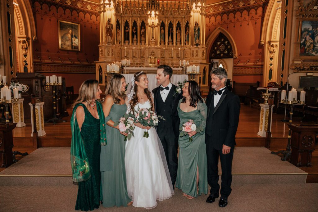 Bride and groom smiling with family standing in church at Quinet Saint John Garden of Our Lady in Massachusetts.