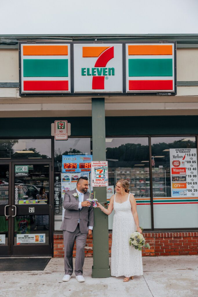 Bride and groom cheering slushies as they lean against pole at 7/11 on their wedding day.