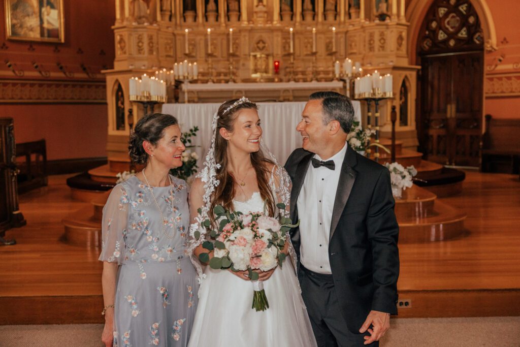 Bride smiling with her mom and dad in church at Quinet Saint John Garden of Our Lady in Massachusetts.