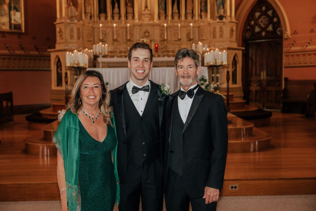 Groom smiling with his parents in church at Quinet Saint John Garden of Our Lady in Massachusetts.