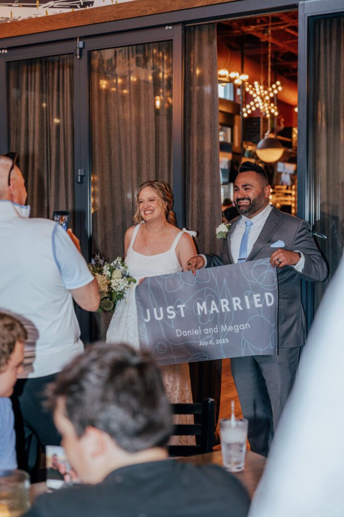 Bride and groom smiling as they enter Citizen Crust in Foxboro, Massachusetts. holding a "Just married" sign.