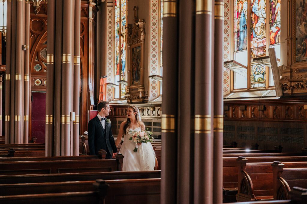 Bride and groom walking through church with stained glass Bride and groom kissing in church at Quinet Saint John Garden of Our Lady in Massachusetts.