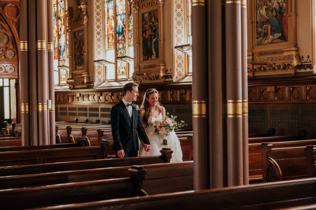 Bride and groom smiling and walking through church during romantic summer wedding at Quinet Saint John Garden of Our Lady in Massachusetts.