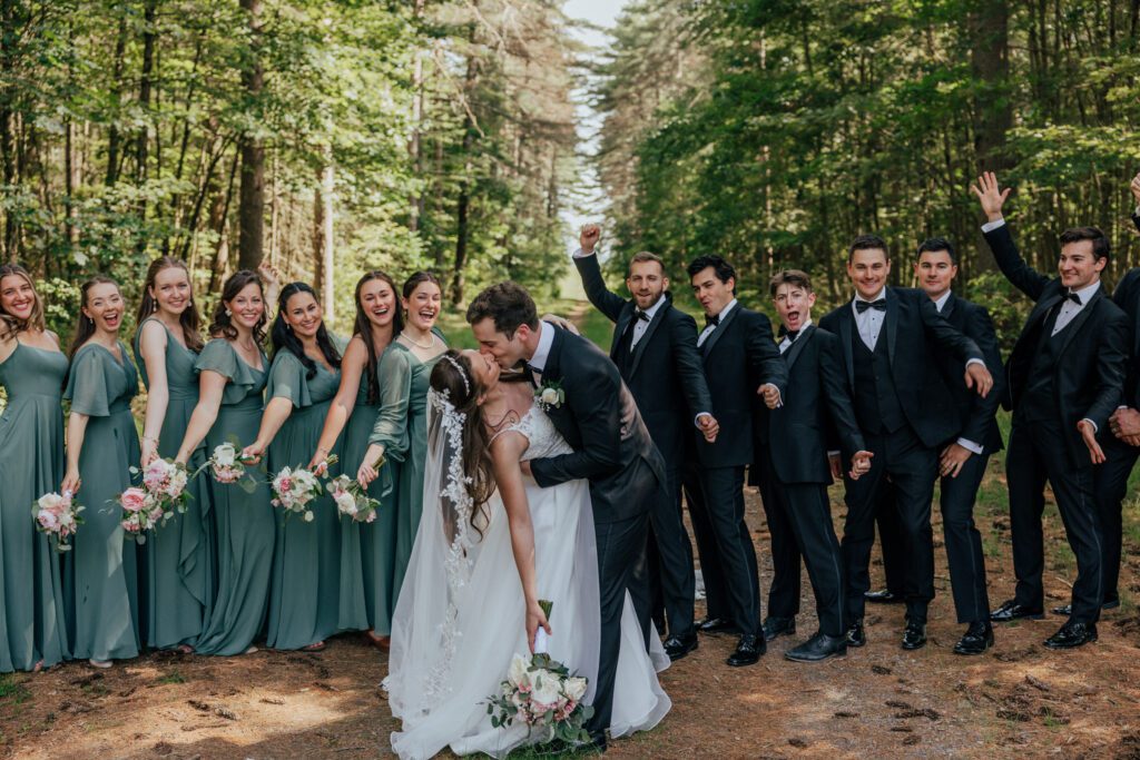 Bridal party cheering at wedding as bride and groom kiss in the woods in Massachusetts.