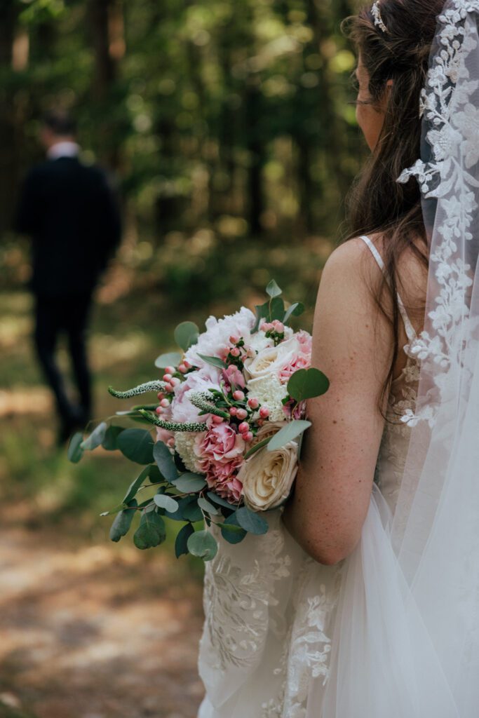 Bride holding pink and white bridal bouquet walking in the woods surrounded by greenery in Massachusetts.