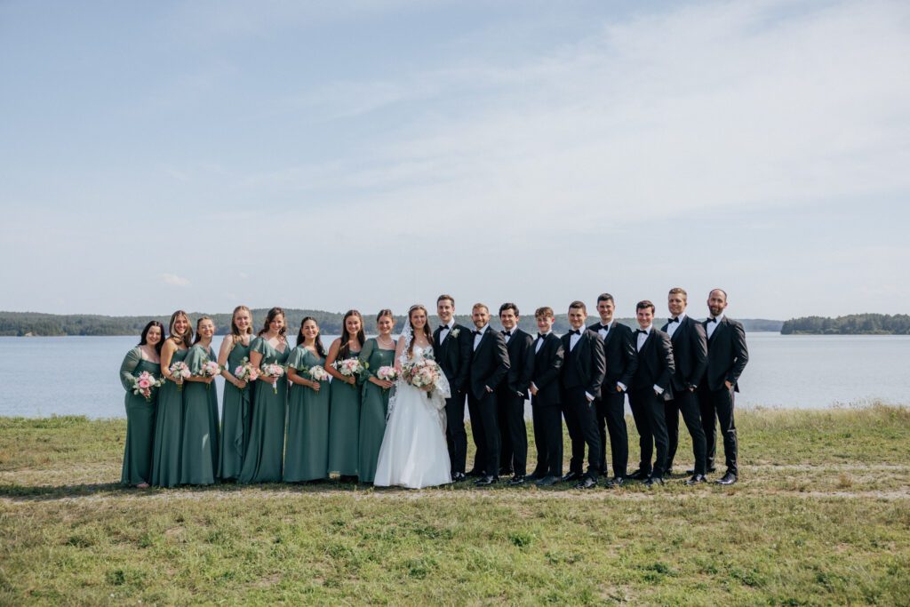 Bridal party standing with bride and groom and smiling in front of pond