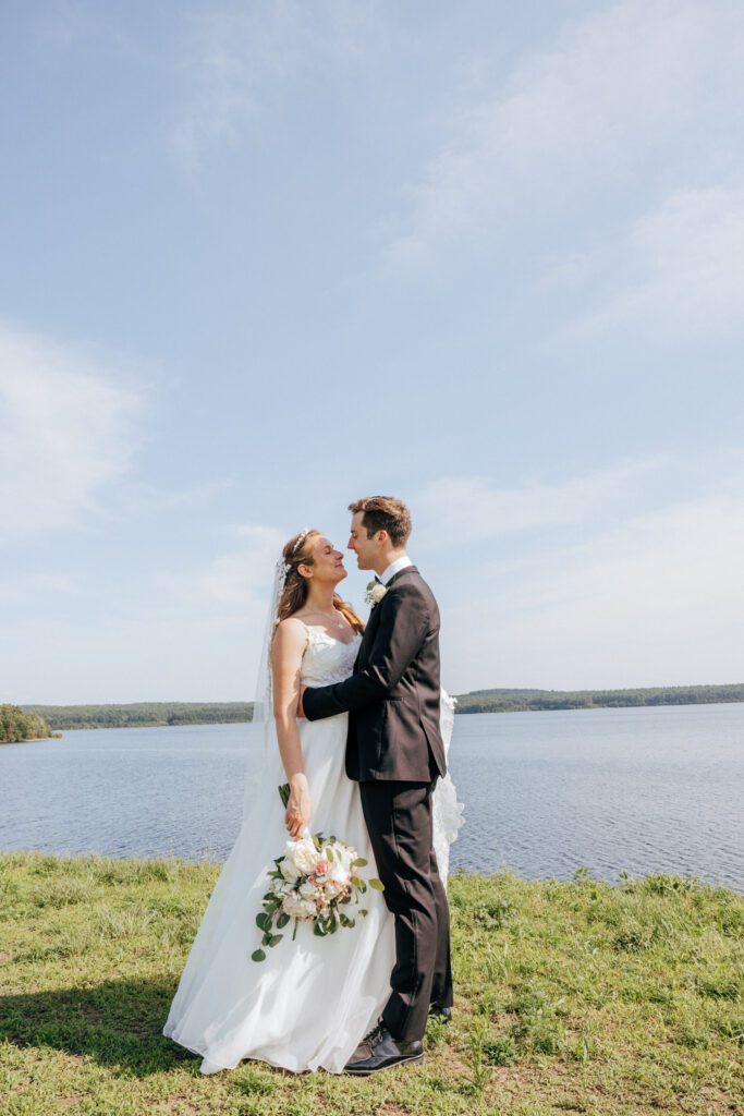 Bride and groom smiling at each other in front of waterfront in Massachusetts.