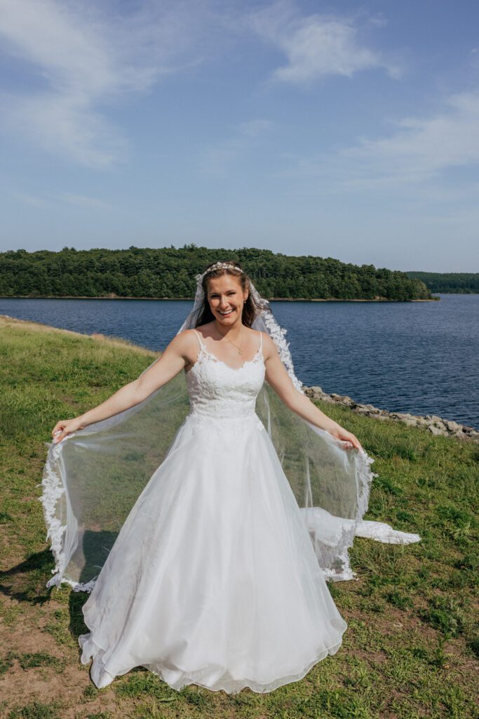 Bride smiling and playing with her veil in front of waterfront in Massachusetts.