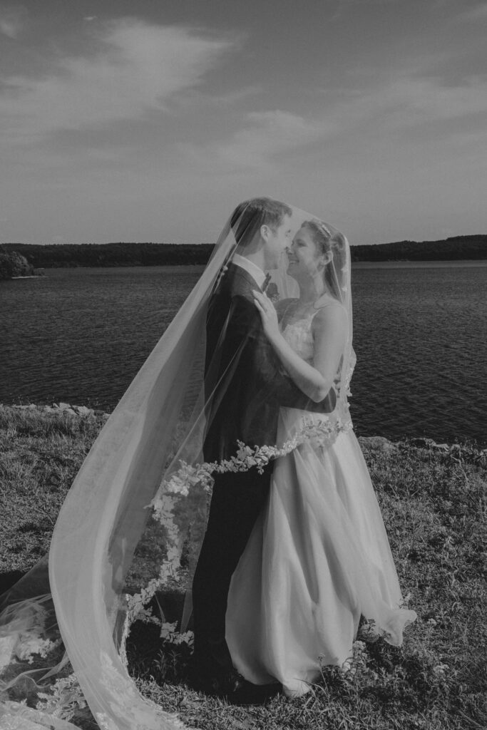 Bride and groom smiling under veil in front of waterfront in Massachusetts.