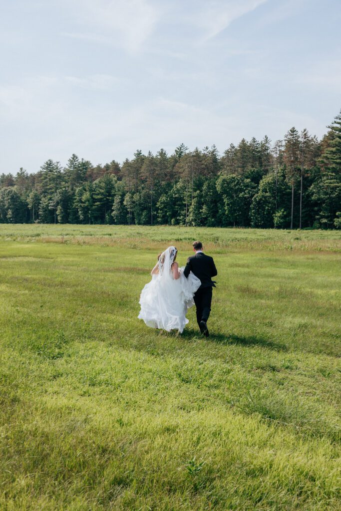 Bride and groom running romantically in field located in Massachusetts.