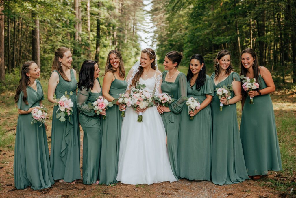 Bride and and bridesmaid standing in a line laughing and smiling in the woods in Massachusetts.