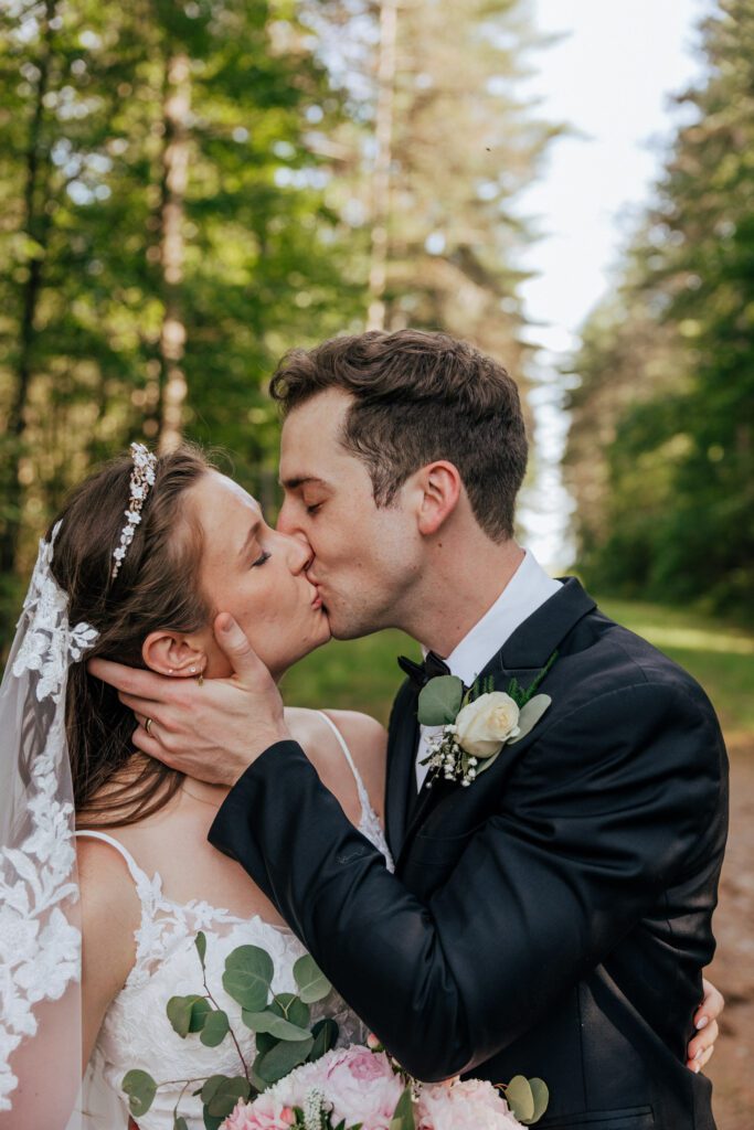 Bride and groom kissing romantically in the wood surrounded by greenery in Massachusetts.