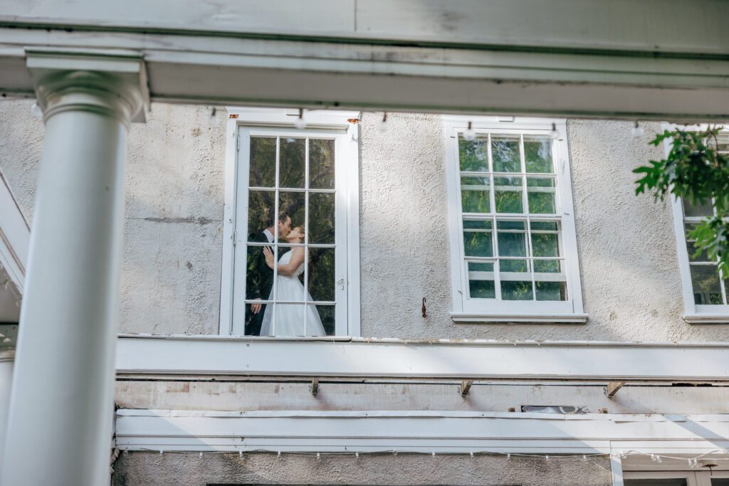 Bride and groom kissing through a window at romantic wedding in Massachusetts.