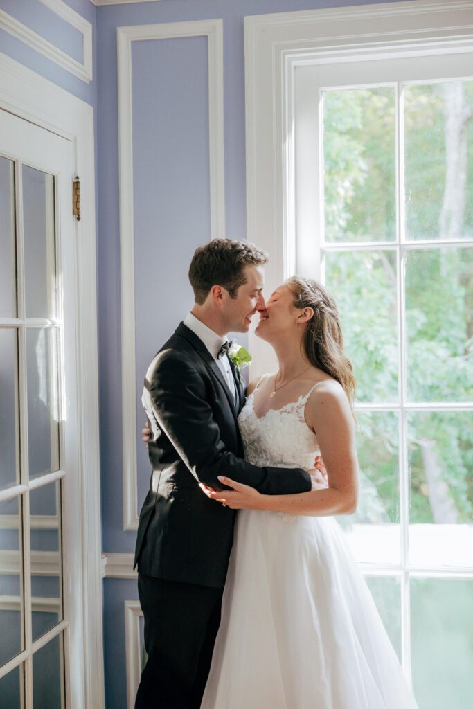 Bride and groom kissing next to a window with romantic sunlight in Massachusetts.