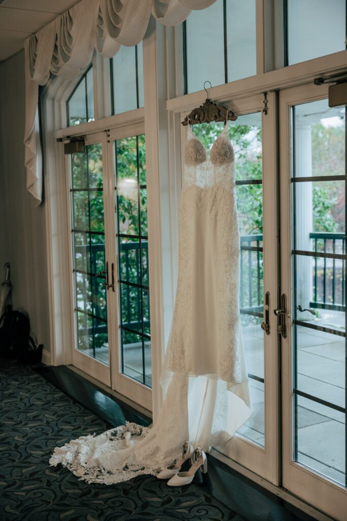 Lace wedding dress hanging on glass door at Black Swan Country Club in Georgetown, Massachusetts.