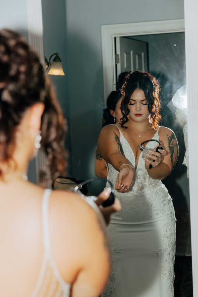 A bride getting ready spraying perfume in a mirror reflection at Black Swan Country Club in Georgetown, Massachusetts.