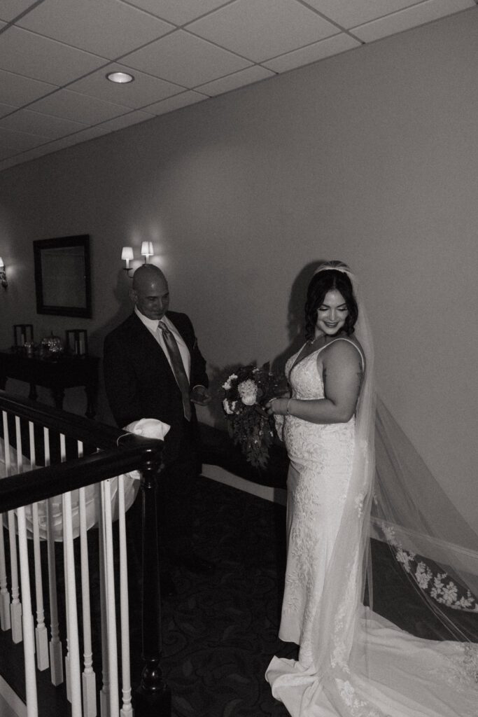 A bride and her father smiling as they look at her wedding dress at Black Swan Country Club in Georgetown, Massachusetts.