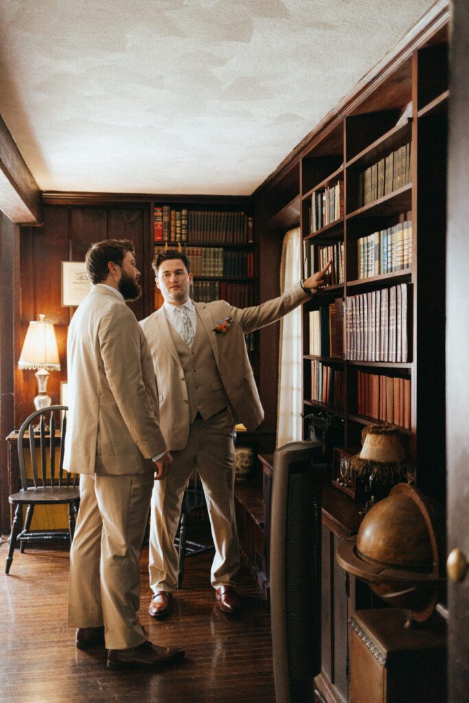 Groom and groomsmen looking at books in the library room at The Evermore at Peirce Farm Estate in Topsfield, Massachusetts.