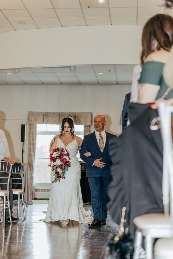 A bride walking down the aisle with her dad at romantic indoor ceremony at Black Swan Country Club in Georgetown, Massachusetts.