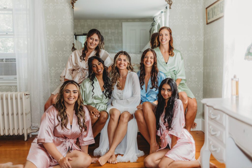 A bride and her bridesmaids smiling in silk robes at The Evermore at Peirce Farm Estate in Topsfield, Massachusetts.