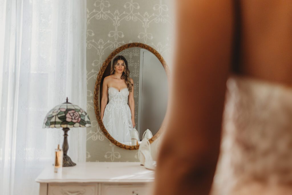 Bride looking at herself in the mirror smiling in her wedding dress at The Evermore at Peirce Farm Estate in Topsfield, Massachusetts.