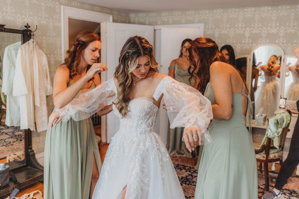Bridesmaids helping the bride put on her dress at The Evermore at Peirce Farm Estate in Topsfield, Massachusetts.