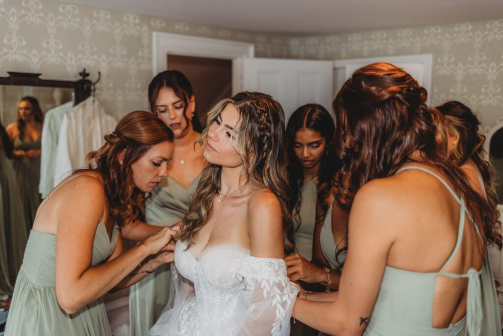 Bridesmaids helping the bride put on her wedding dress sleeves at The Evermore at Peirce Farm Estate in Topsfield, Massachusetts.