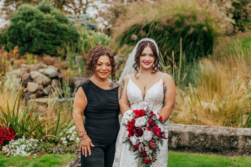 A bride and her mother smiling outside in front of greenery at Black Swan Country Club in Georgetown, Massachusetts.