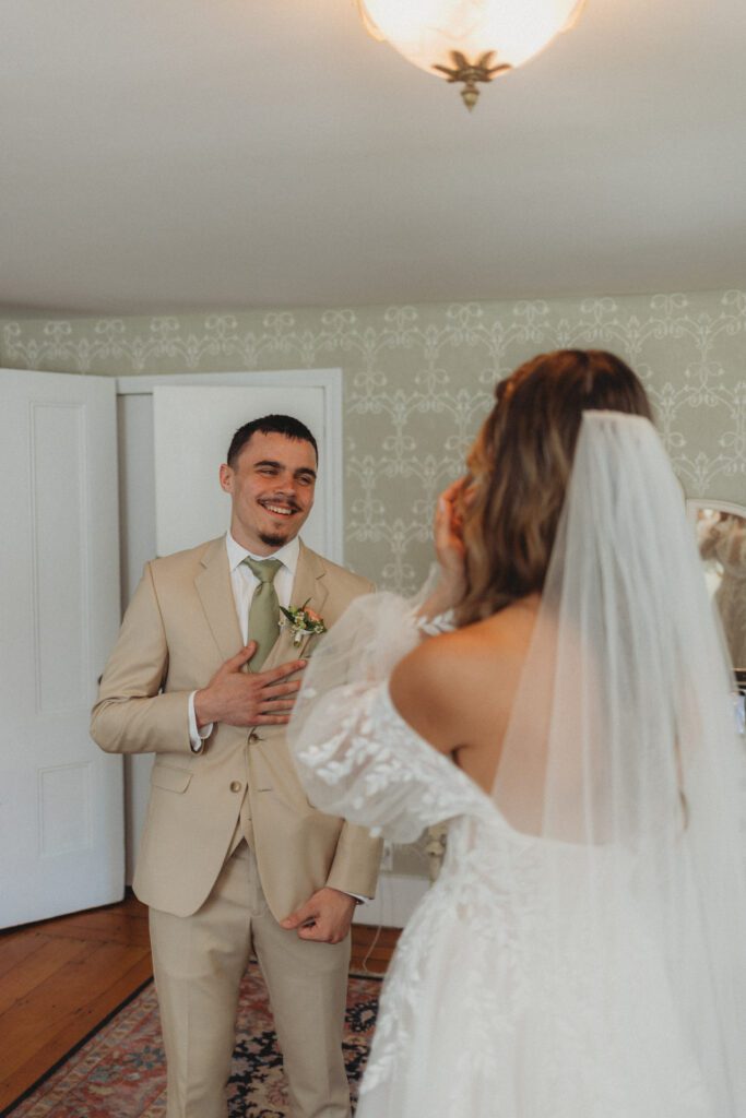 Bride's brother smiling with his hand on his chest during a first look with the bride at The Evermore at Peirce Farm Estate in Topsfield, Massachusetts.