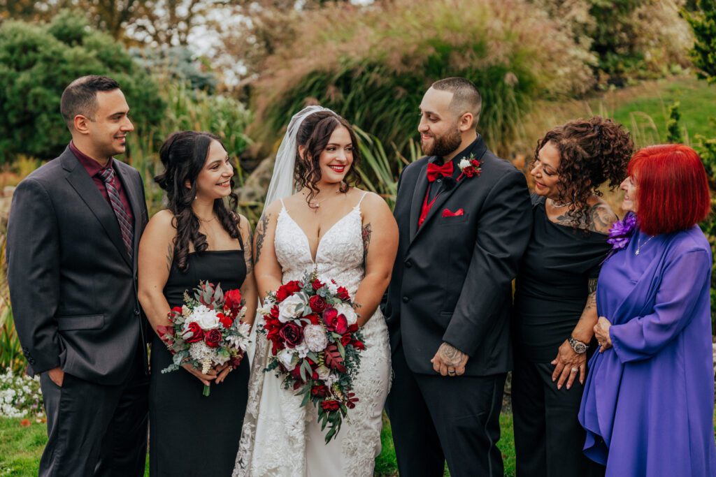 Bride and groom smiling with family standing outside in front of greenery at Black Swan Country Club in Georgetown, Massachusetts.