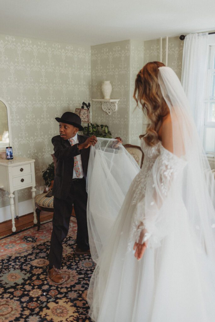 Bride's younger brother touching her dress during a first look at The Evermore at Peirce Farm Estate in Topsfield, Massachusetts.