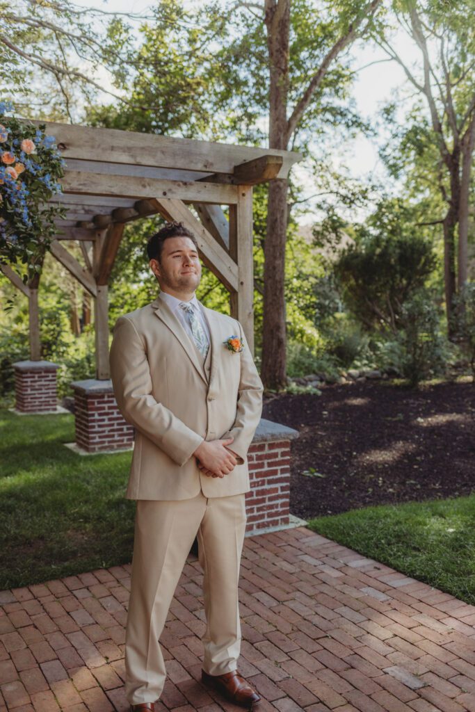 Groom smiling as bride walks towards him during a whimsical outdoor wedding ceremony at Peirce Farm Estate in Topsfield, Massachusetts.