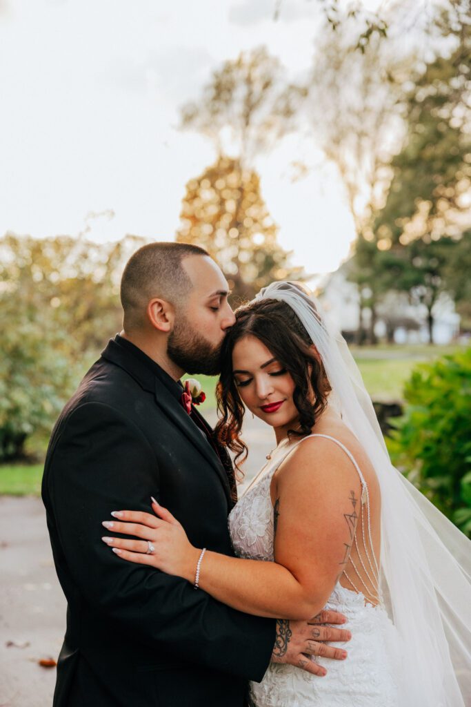 Groom kissing bride on the head outside during romantic fall wedding at Black Swan Country Club in Georgetown, Massachusetts.