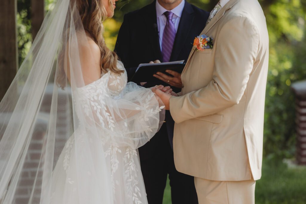 Close up of bride and groom sweetly holding hands during outdoor wedding ceremony at Peirce Farm Estate in Topsfield, Massachusetts.