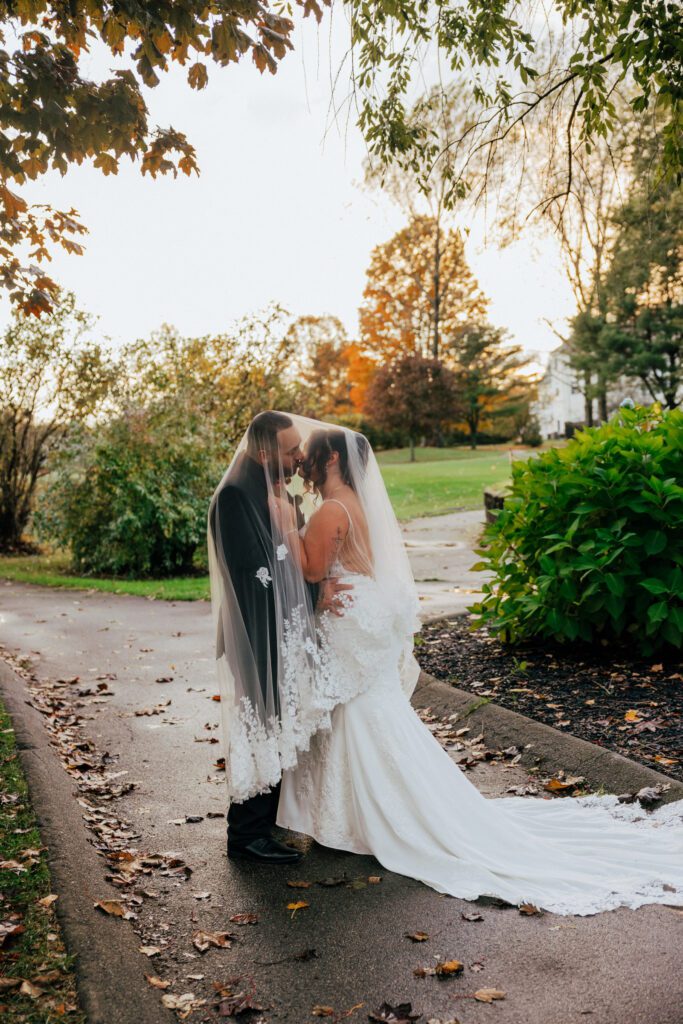 Fall wedding with bride and groom kissing under wedding veil outside at Black Swan Country Club in Georgetown, Massachusetts.