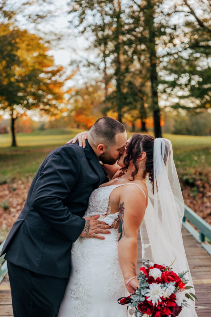 Groom and bride kissing outside on wooden bridge during fall wedding at Black Swan Country Club in Georgetown, Massachusetts.