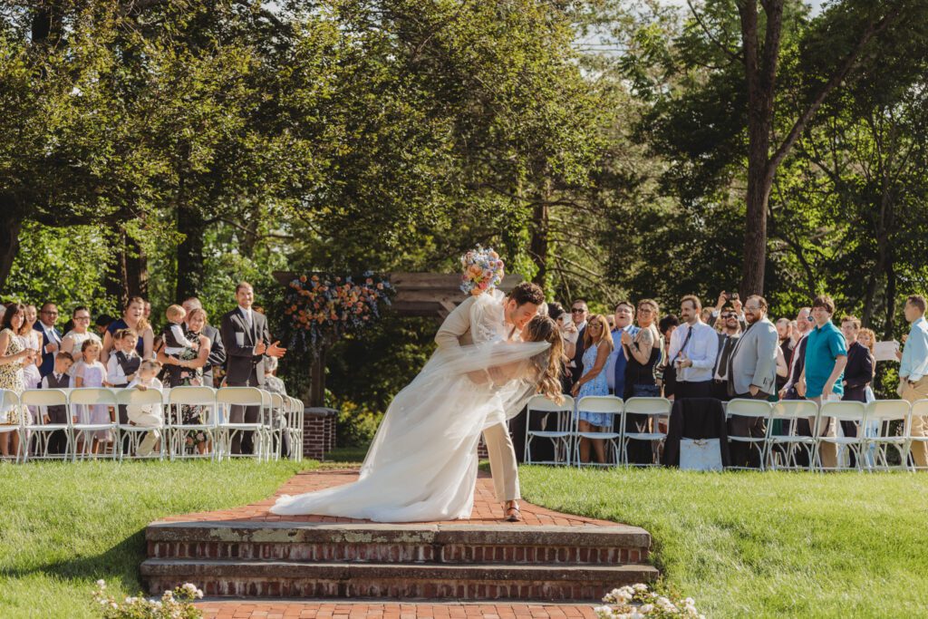 Groom dipping the bride are kissing twith their guest smiling and clapping behind them at Peirce Farm Estate in Topsfield, Massachusetts.