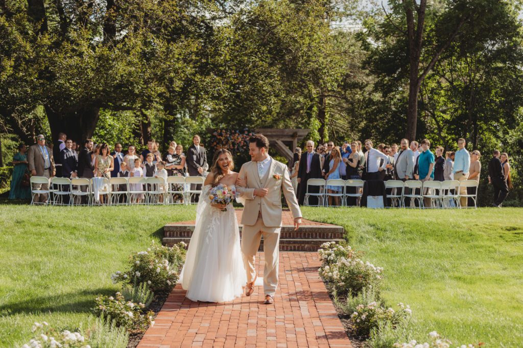 Bride and groom walk down the aisle together with their guests smiling behind them at Peirce Farm Estate in Topsfield, Massachusetts.