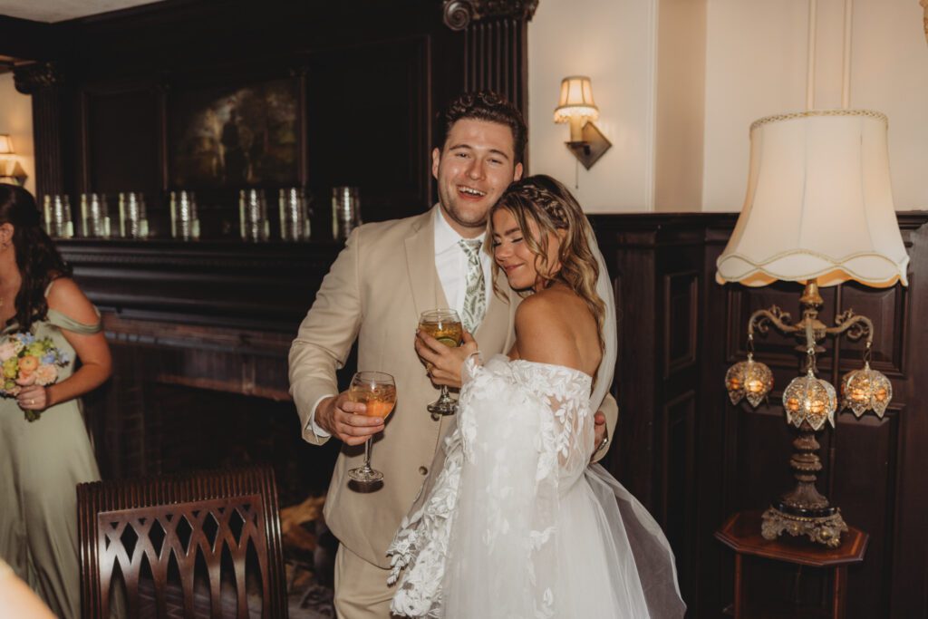 Groom is hugging bride as they are holding wine glasses in a charming room at Peirce Farm Estate in Topsfield, Massachusetts.