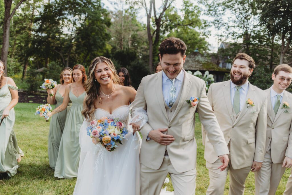 Bridal party walks behind bride and groom as they are laughing and walking outside at Peirce Farm Estate in Topsfield, Massachusetts.