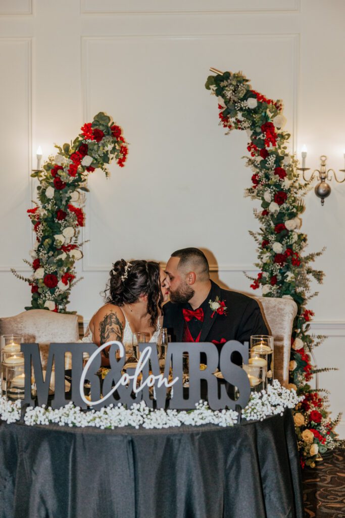 Bride and groom kissing during wedding reception with flower arch behind them at Black Swan Country Club in Georgetown, Massachusetts.