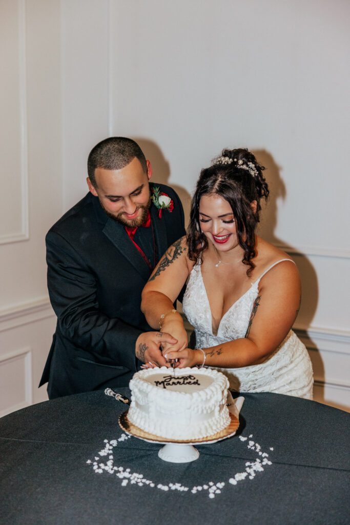 Bride and groom cutting wedding cake and smiling during wedding reception at Black Swan Country Club in Georgetown, Massachusetts.