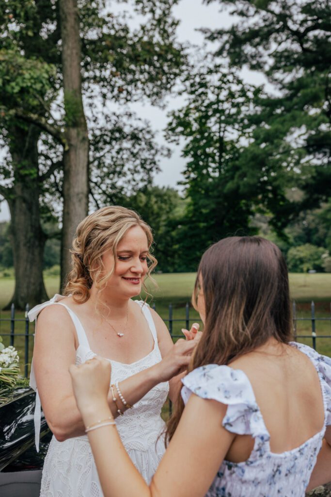 Bride and daughter smiling as they get ready at Bird Park in Walpole, Massachusetts in the summer.